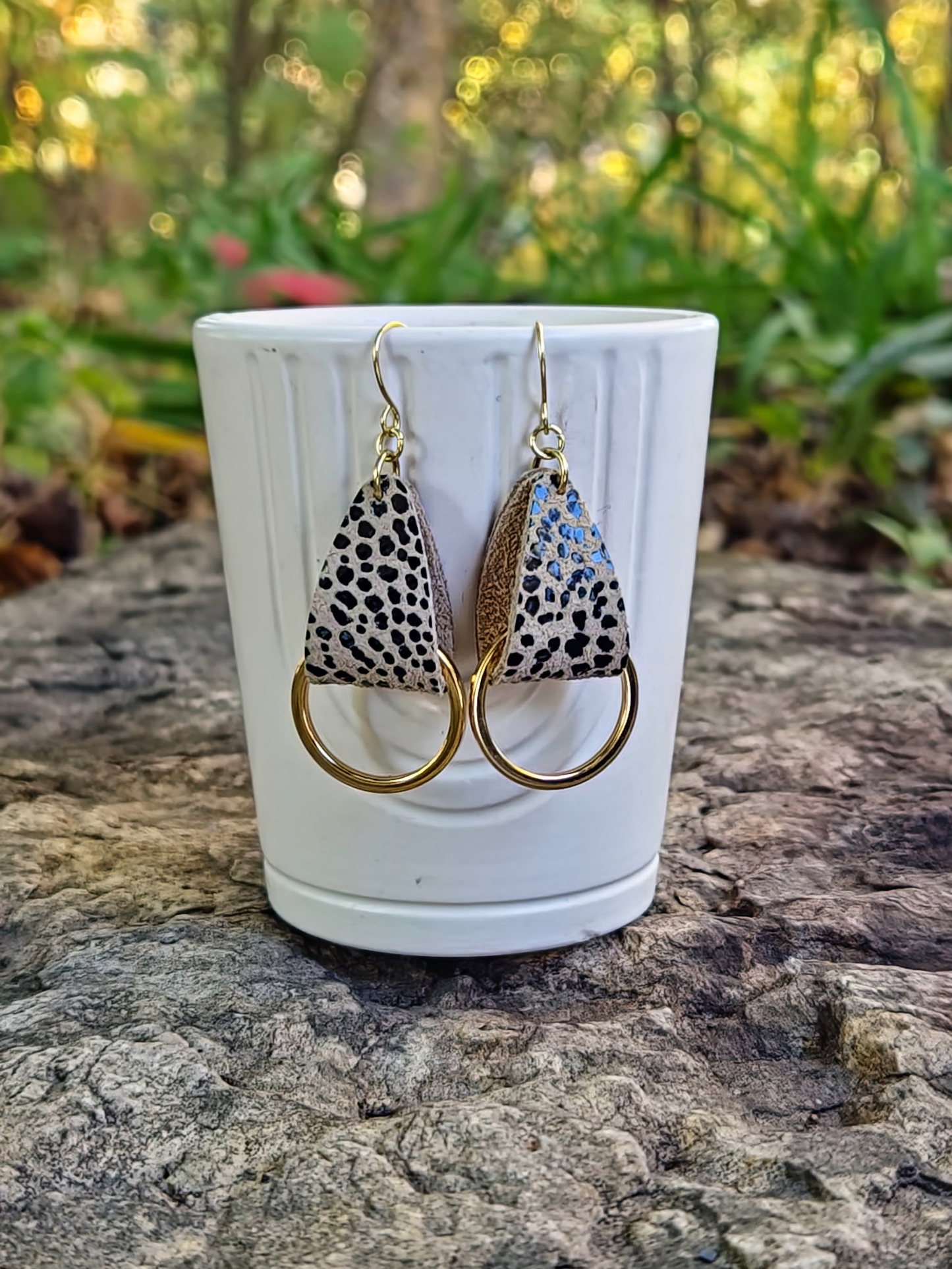 Pair of earrings with animal print design on a white cup against a natural background