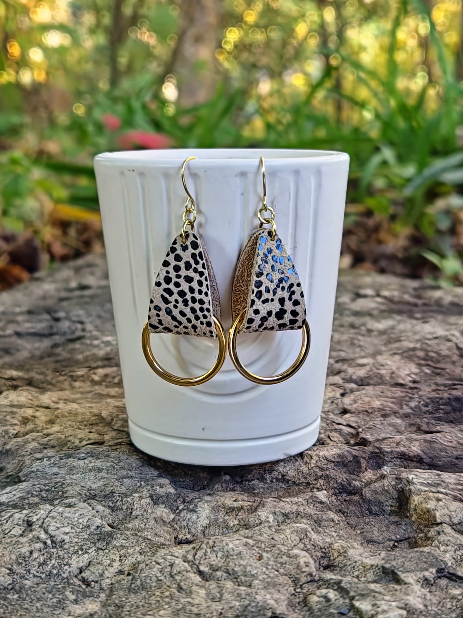 Pair of earrings with animal print design on a white cup against a natural background
