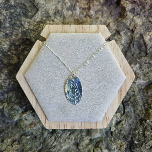 Necklace with a leaf-shaped pendant on a hexagonal wooden stand against a stone background